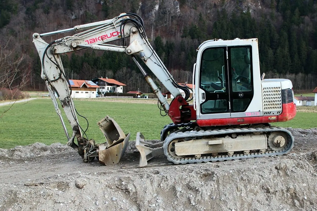 White compact excavator with its bucket lowered on a dirt site